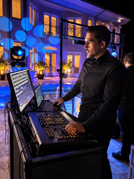 A lighting technician operating a professional console beside the pool during an evening event.