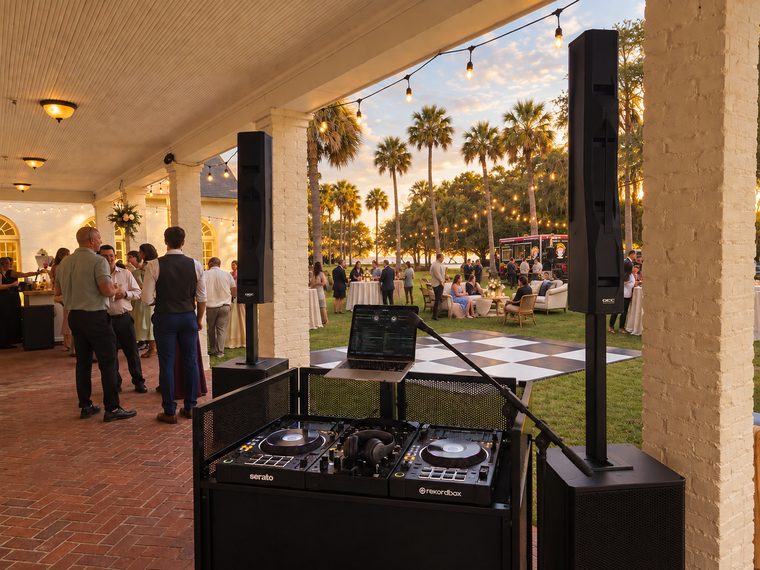 DJ booth and column-array systems overlooking an outdoor reception at sunset