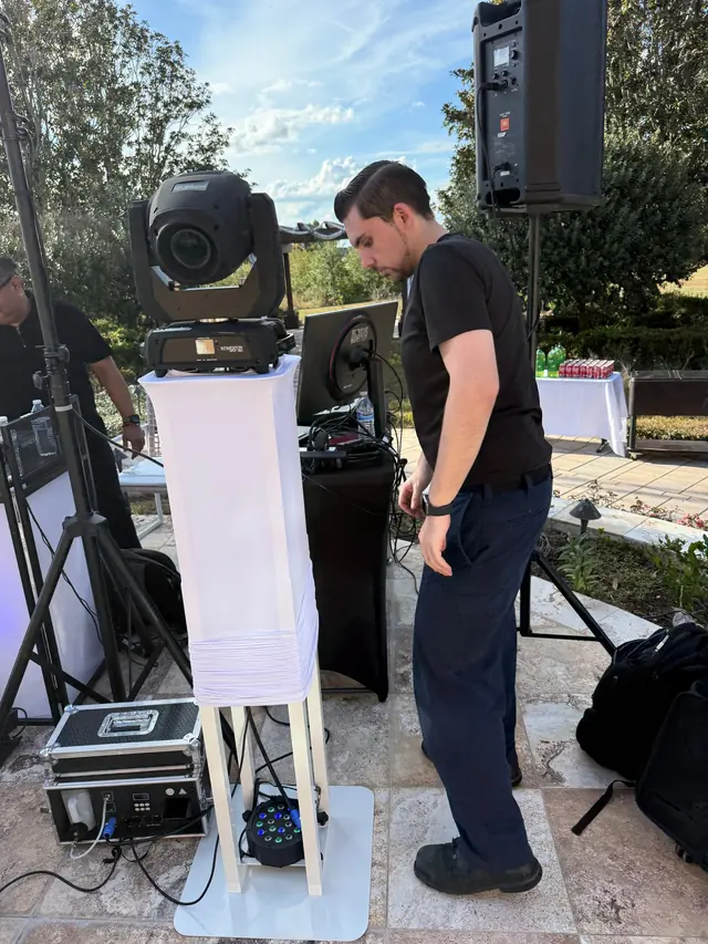 Technician checking cables beside a speaker and moving-head light